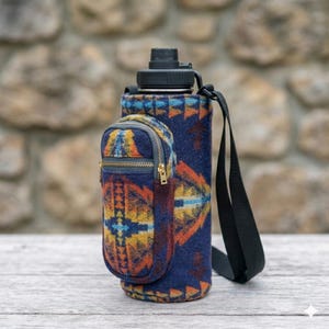 May include: A navy blue water bottle with a black lid and strap, encased in a patterned fabric sleeve. The sleeve features a geometric design in orange, yellow, and blue. A small zippered pouch is attached to the side.