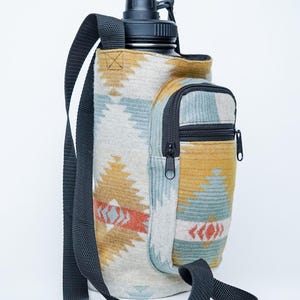 May include: A water bottle carrier with a black strap and a small zipped pocket. The carrier features a geometric pattern in beige, blue, orange, and yellow. The water bottle has a black lid.
