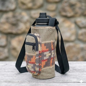 May include: A water bottle with a black lid and a patterned fabric sleeve. The sleeve has a small zippered pouch and a black shoulder strap. The fabric design includes orange, red, and tan geometric shapes.