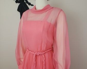 May include: A long, pink, sheer dress with a high neck and long sleeves. The dress has a pleated skirt and a braided belt with beaded accents.