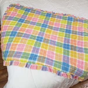 May include: A pink, yellow, blue, and green plaid quilted throw blanket with a ruffled edge.