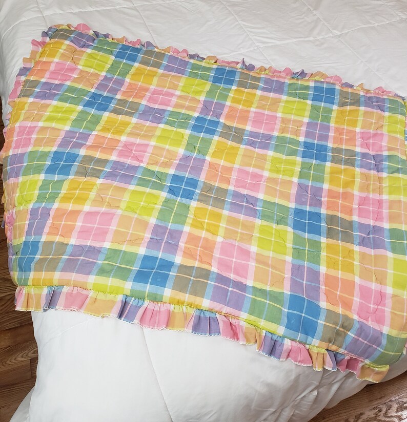 May include: A pink, yellow, blue, and green plaid quilted throw blanket with a ruffled edge.