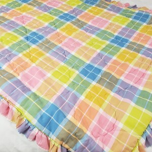 May include: A colorful plaid quilt with a ruffled edge. The quilt is made of a soft, cotton fabric and features a variety of pastel colors, including pink, blue, yellow, and green.