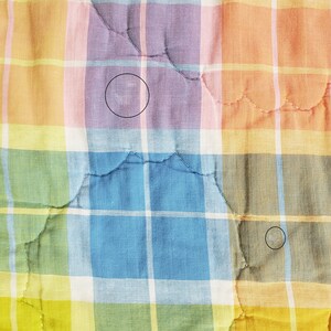 May include: A multi-colored plaid fabric with a quilted pattern. The fabric has a light pink, light orange, light yellow, light green, and light blue plaid pattern. The fabric is quilted with a wavy pattern.