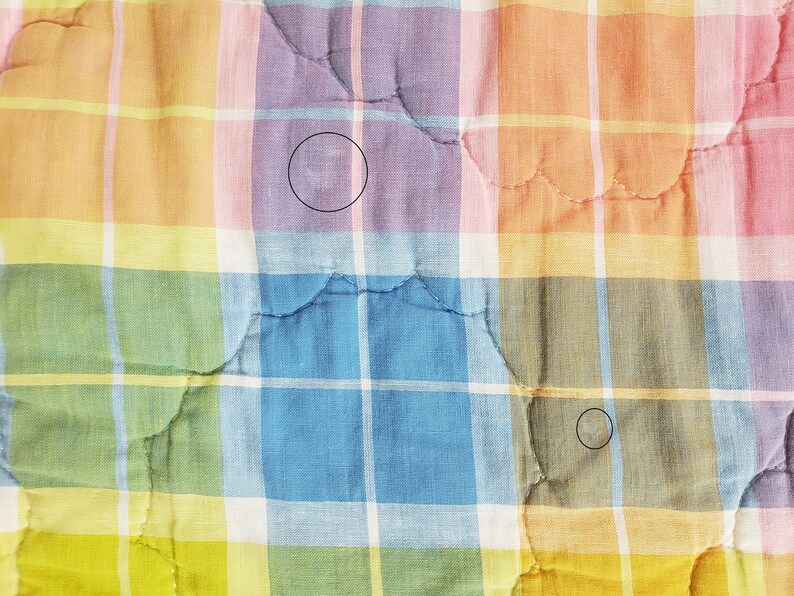 May include: A multi-colored plaid fabric with a quilted pattern. The fabric has a light pink, light orange, light yellow, light green, and light blue plaid pattern. The fabric is quilted with a wavy pattern.