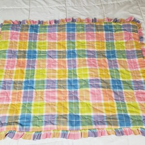 May include: A pastel plaid quilted throw blanket with a ruffled edge. The blanket is made of soft cotton and features a variety of colors, including pink, yellow, blue, and green.