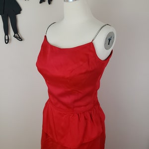 May include: A red satin dress with a fitted skirt and a ruffled peplum. The dress has thin straps with rhinestones.