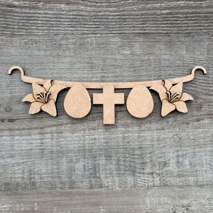 May include: A wooden Easter banner featuring a cross, two eggs, and two lilies. The banner is made of light brown wood and has a decorative design. The banner is designed to be hung and is perfect for Easter decorations.