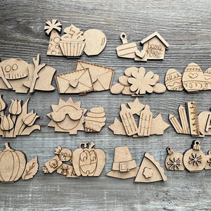 May include: A set of 19 unfinished wooden cutouts featuring various shapes and designs, including a pumpkin, a graduation cap, a house, a flower, a ruler, and a letter A. The cutouts are perfect for crafting and decorating.