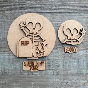 May include: Wooden Halloween decorations featuring a skeleton, pumpkin, and tombstone with the letters "RIP." The text "Shakin' in my bones" is included. A smaller decoration shows a skeleton and the word "Spooky."