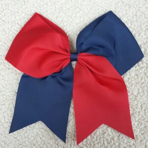 May include: A large, handmade cheerleading bow in a patriotic color scheme. The bow features a vibrant red and navy blue color combination. The bow is made of a sturdy, textured ribbon and has a classic bow shape.