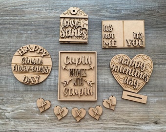 May include: A set of wooden Valentine's Day decorations with various sayings, including "Happy Single Awareness Day", "Cupid Rhymes with Stupid", "It's not me, it's you", and "Happy Valentine's Day".