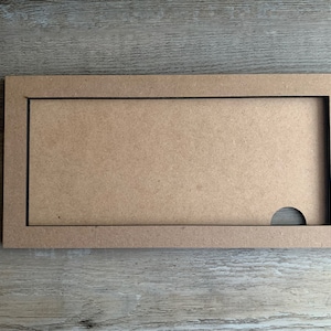 May include: A rectangular wooden frame with a cutout in the lower right corner. The frame is made of light brown wood and has a dark brown border.