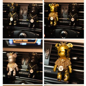 May include: Four car air fresheners shaped like bears wearing crowns and jeweled necklaces. The bears are black, silver, and gold. The gold bear has the letters "W", "ACE", and "LOV" on it. The black bears have the letter "M" on them. The silver bear has the letter "Y" on it.