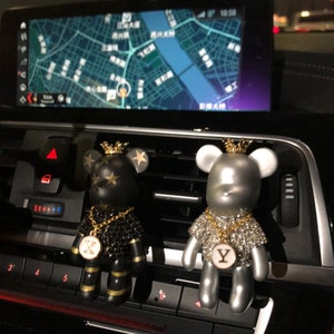 May include: Two car air fresheners shaped like bears wearing gold chains and crowns. The bear on the left is black with gold stars and a gold 'X' pendant. The bear on the right is silver with rhinestones and a gold 'Y' pendant.