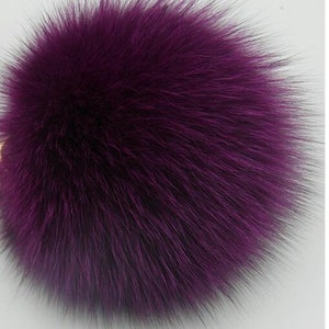 May include: A large, fluffy purple pom pom made of faux fur. The pom pom is soft and plush, and would be perfect for adding a touch of whimsy to a hat, scarf, or bag.
