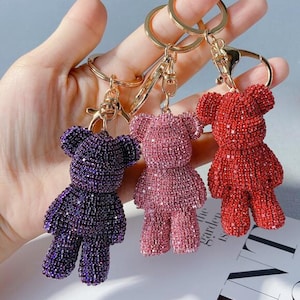 May include: Three sparkly teddy bear keyrings in purple, pink and red. Each keyring features a gold metal ring and a lobster clasp.