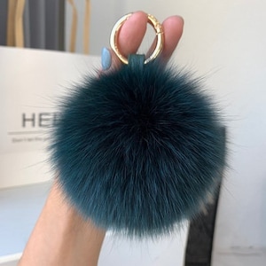 May include: A dark green fluffy pom pom keychain with a gold ring.
