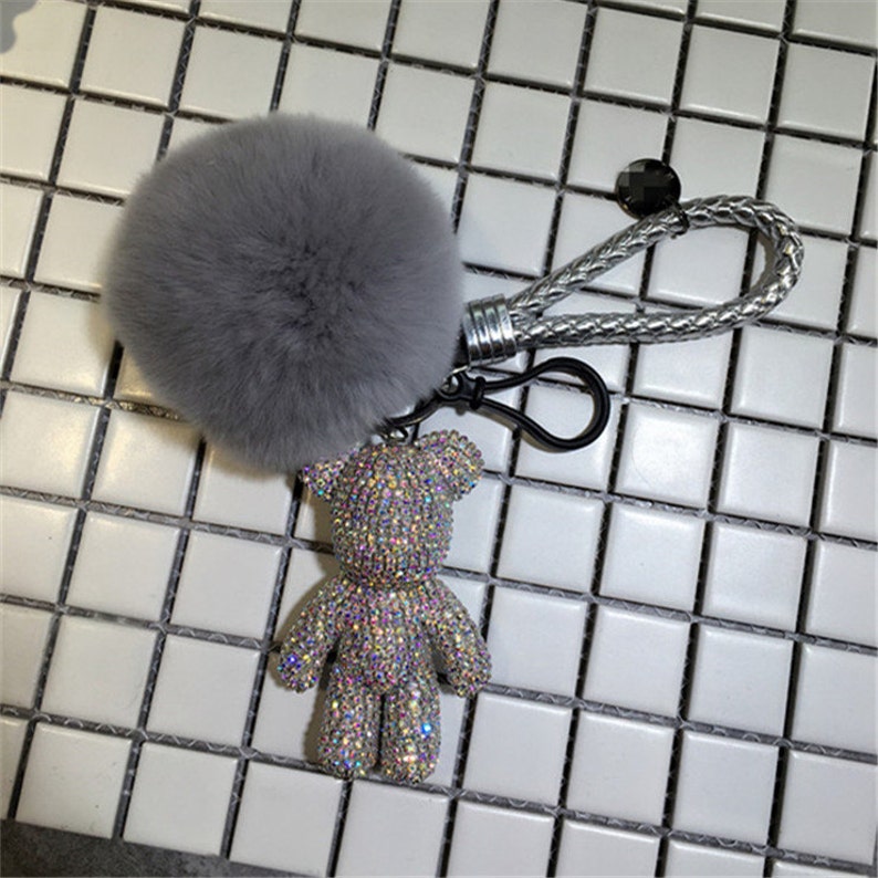 May include: A gray fluffy pom-pom keychain with a silver chain and a sparkly rhinestone bear charm.