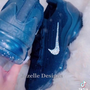 May include: A pair of blue Nike trainers with a white swoosh and a sparkly design. The trainers are decorated with rhinestones. The text "Jezelle Designs" is visible on the image. The text "#jezelledesigns #BLINGBLING" is also visible on the image.
