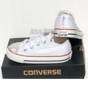 Peut inclure: Des baskets Converse All-Star blanches avec une bande rouge et un logo &eacute;toile bleue. Les chaussures sont d&eacute;cor&eacute;es de strass sur la pointe et &agrave; l'arri&egrave;re.