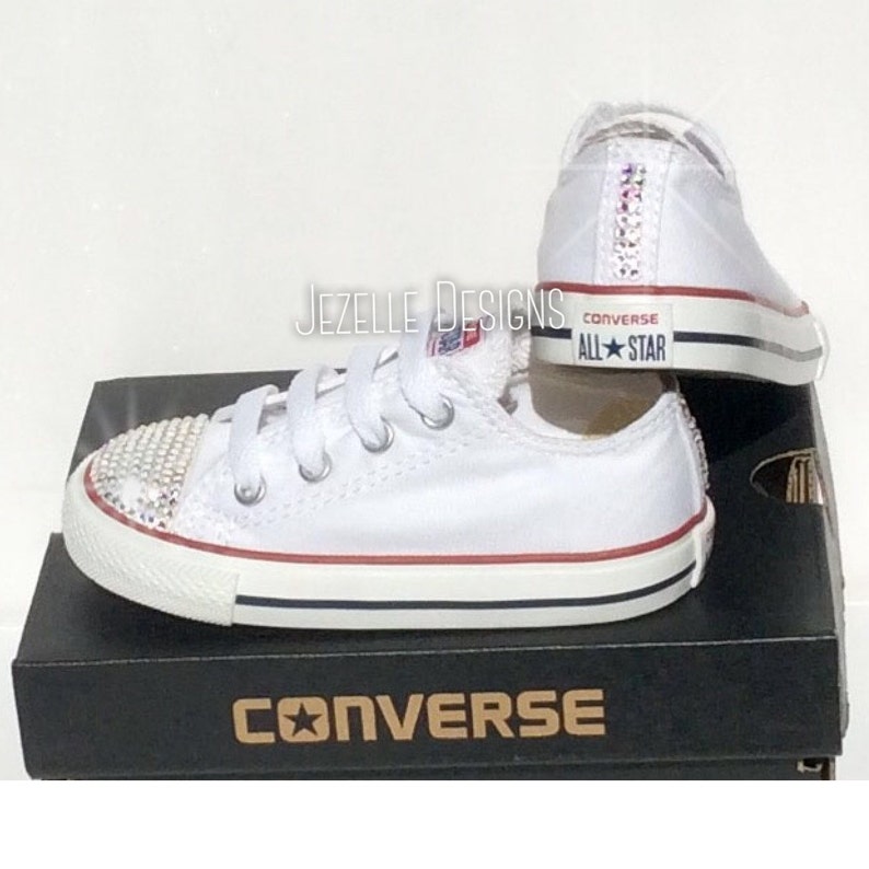 Peut inclure: Des baskets Converse All-Star blanches avec une bande rouge et un logo &eacute;toile bleue. Les chaussures sont d&eacute;cor&eacute;es de strass sur la pointe et &agrave; l'arri&egrave;re.