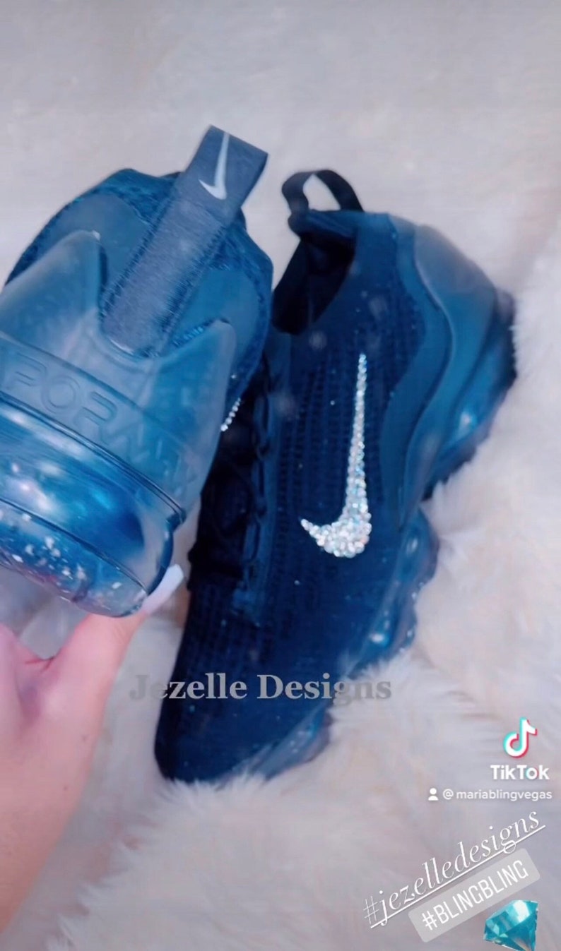 May include: A pair of blue Nike trainers with a white swoosh and a sparkly design. The trainers are decorated with rhinestones. The text "Jezelle Designs" is visible on the image. The text "#jezelledesigns #BLINGBLING" is also visible on the image.