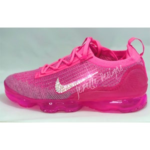 May include: Pink Nike trainers with a clear sole and a crystal-encrusted swoosh logo. The text "Jezelle Designs" is visible on the side of the shoe.