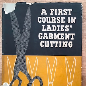 May include: A book cover with the title "A First Course in Ladies' Garment Cutting" in white text on a black background. A large pair of scissors with a gray and white pattern is on the cover, partially obscuring the title. The background is yellow with five smaller scissors in white.