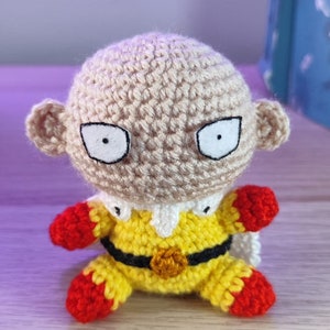 Peut inclure: Figurine au crochet de Saitama, personnage de One-Punch Man. Il porte un costume jaune et noir avec des gants et des bottes rouges. Le personnage a le crâne chauve et une expression sérieuse. Fait à la main.