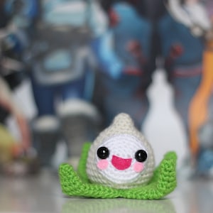 May include: A crocheted plush toy of a white character with green leaves. The character has large black eyes, a pink mouth, and rosy cheeks.