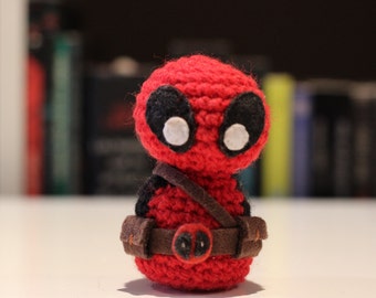 Op de afbeelding: Een rood gebreid Deadpool-personage met zwarte ogen en een bruine riem.