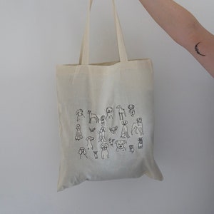 May include: A white canvas tote bag with black line drawings of various dog breeds. The bag has two long straps.
