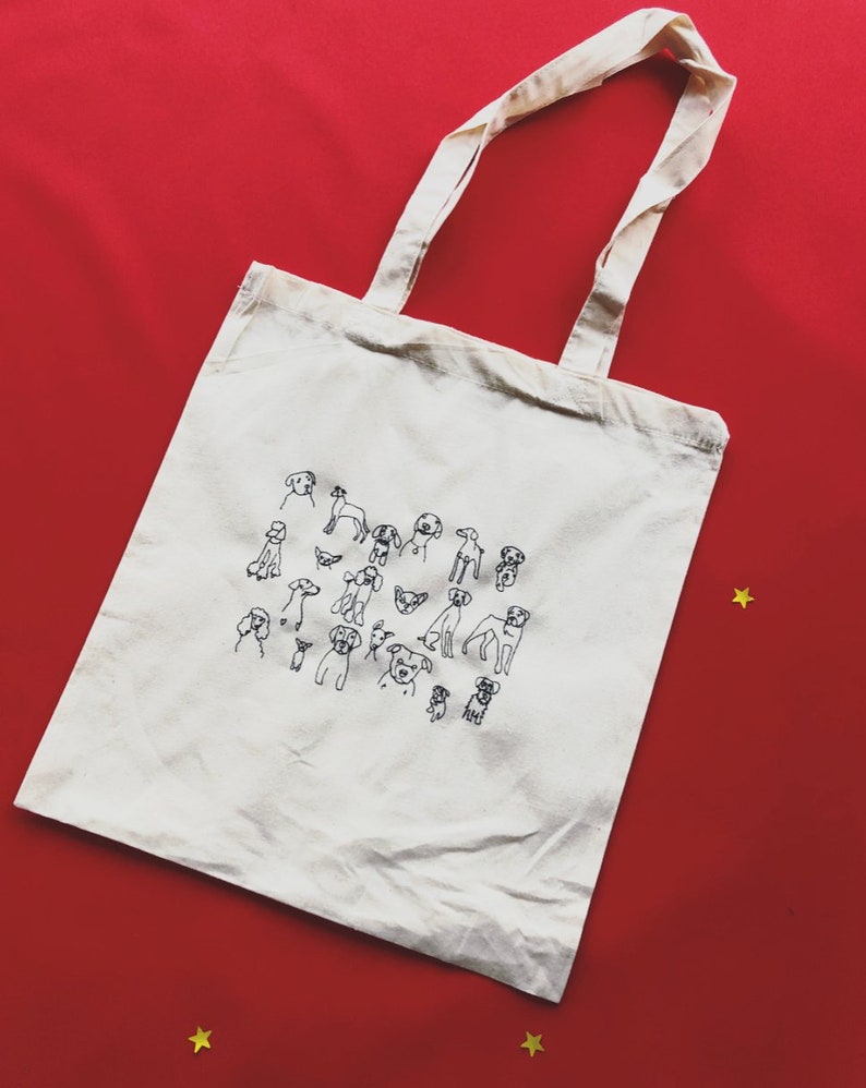 May include: A white canvas tote bag with black line drawings of various dog breeds. The bag has two long handles.