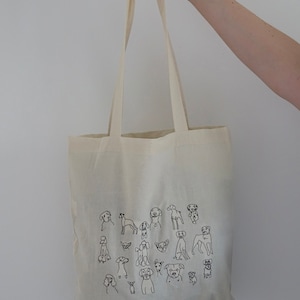 May include: A white canvas tote bag with black line drawings of various dog breeds. The bag has two long handles.