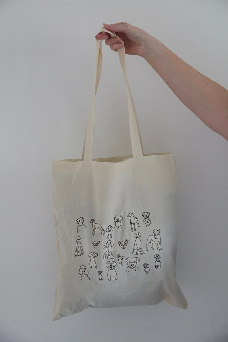 May include: A white canvas tote bag with black line drawings of various dog breeds. The bag has two long handles.
