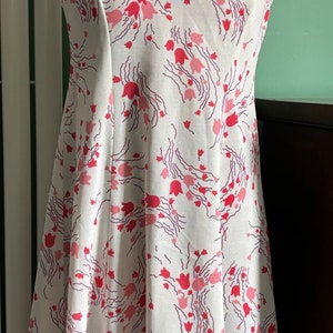 Pode incluir: Um vestido branco sem mangas com estampa floral rosa e roxo. O vestido tem um corpete ajustado e uma saia rodada.