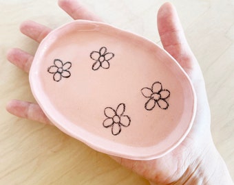 May include: A pink ceramic dish with a scalloped edge and four black flower designs.