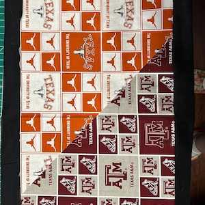 Puede incluir: Dos paneles de tela con patrones repetidos. El panel superior es naranja y blanco con las palabras "The University of Texas" y "Texas" repetidas. El panel inferior es marrón y blanco con las palabras "Texas A&M" repetidas.