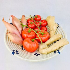 May include: A woven basket with a blue and white pattern holds a variety of fresh produce, including red tomatoes, shallots, and ginger.