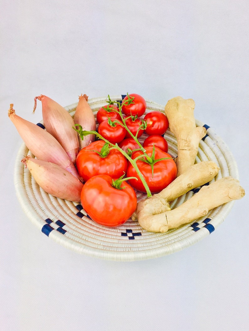 May include: A woven basket with a blue and white pattern holds a variety of fresh produce, including red tomatoes, shallots, and ginger.