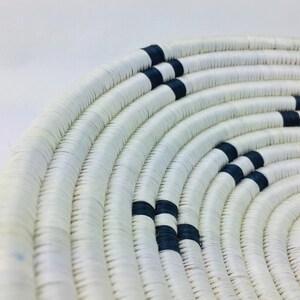 May include: A white woven basket with black stripes. The basket is round and has a wide opening.