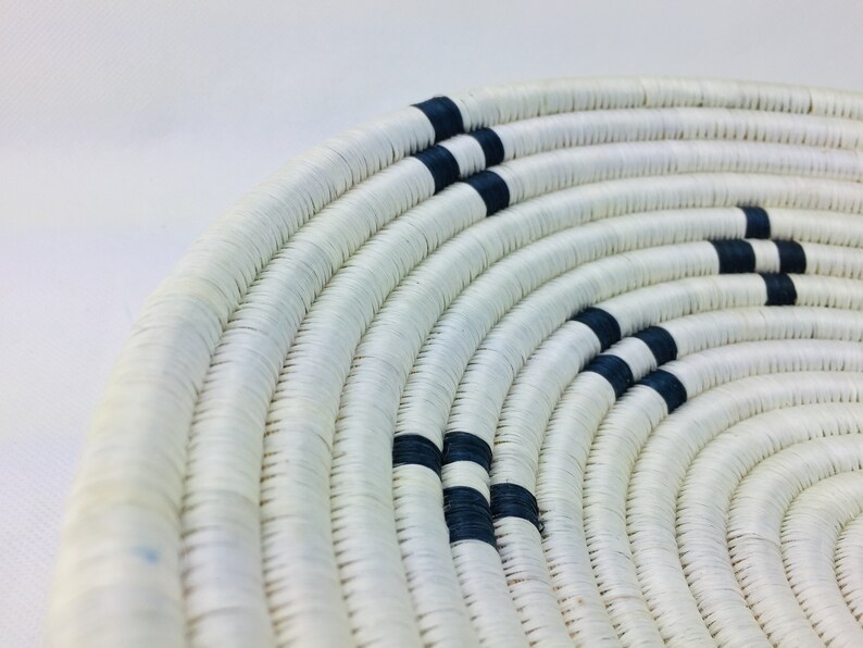 May include: A white woven basket with black stripes. The basket is round and has a wide opening.