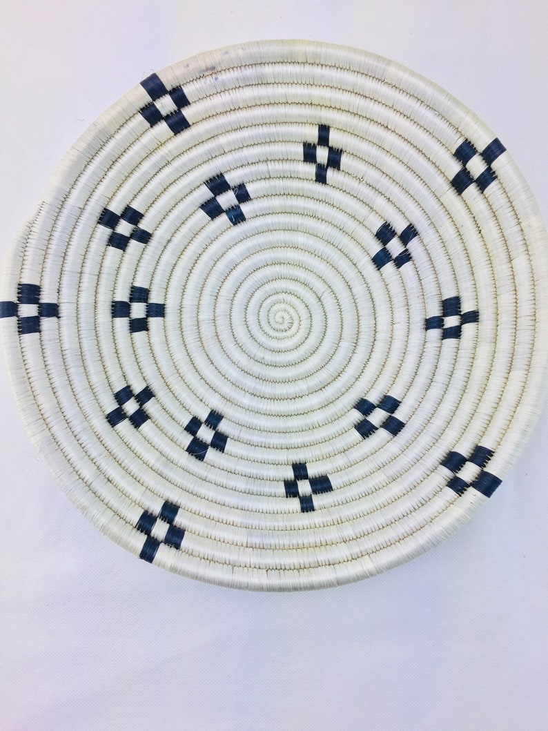 May include: A white woven basket with a black geometric pattern. The basket is round and has a flat bottom.