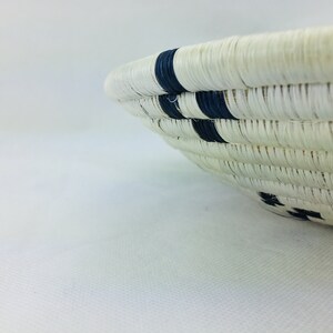 May include: A white woven basket with black stripes. The basket is round and has a wide opening.