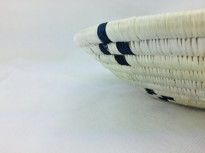 May include: A white woven basket with black stripes. The basket is round and has a wide opening.