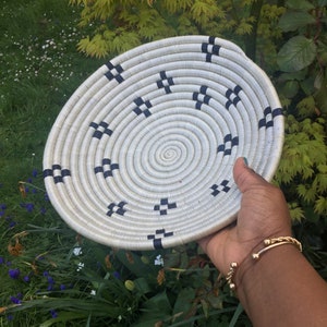 May include: A white woven basket with a black and white geometric pattern. The basket is round and has a flat bottom.