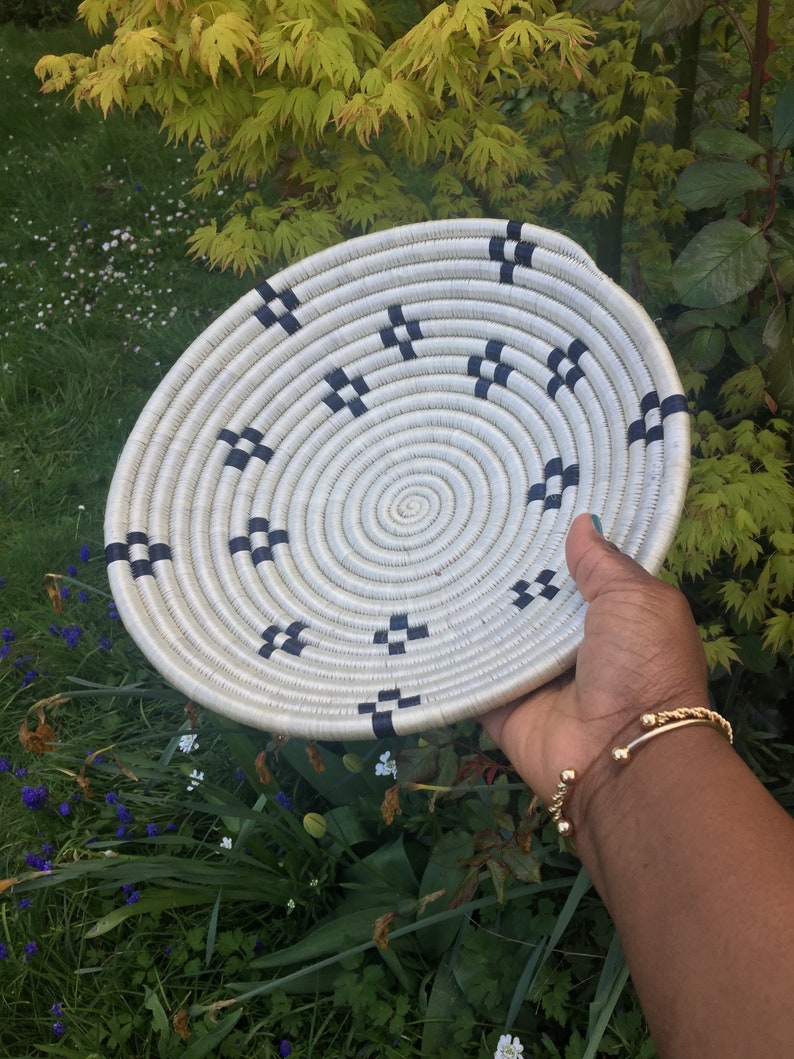 May include: A white woven basket with a black and white geometric pattern. The basket is round and has a flat bottom.