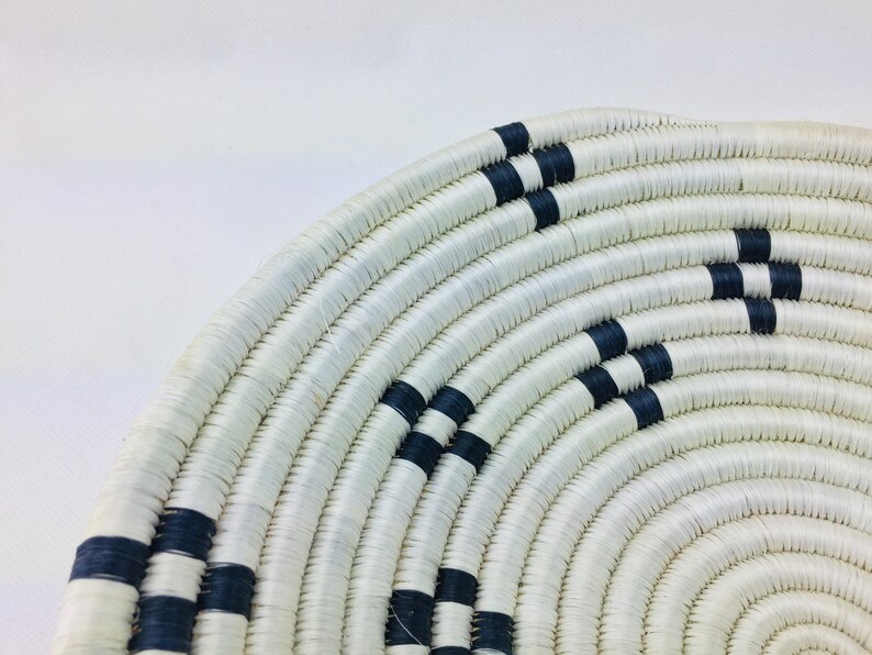 May include: A white woven basket with black stripes. The basket is round and has a wide opening. It is made of natural materials and has a rustic look.