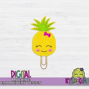 May include: A yellow pineapple-shaped paper clip with a smiling face, pink cheeks, and a pink bow. The pineapple has a green leafy top and is made of felt. The text "DIGITAL MACHINE EMBROIDERY DESIGN" is at the bottom.